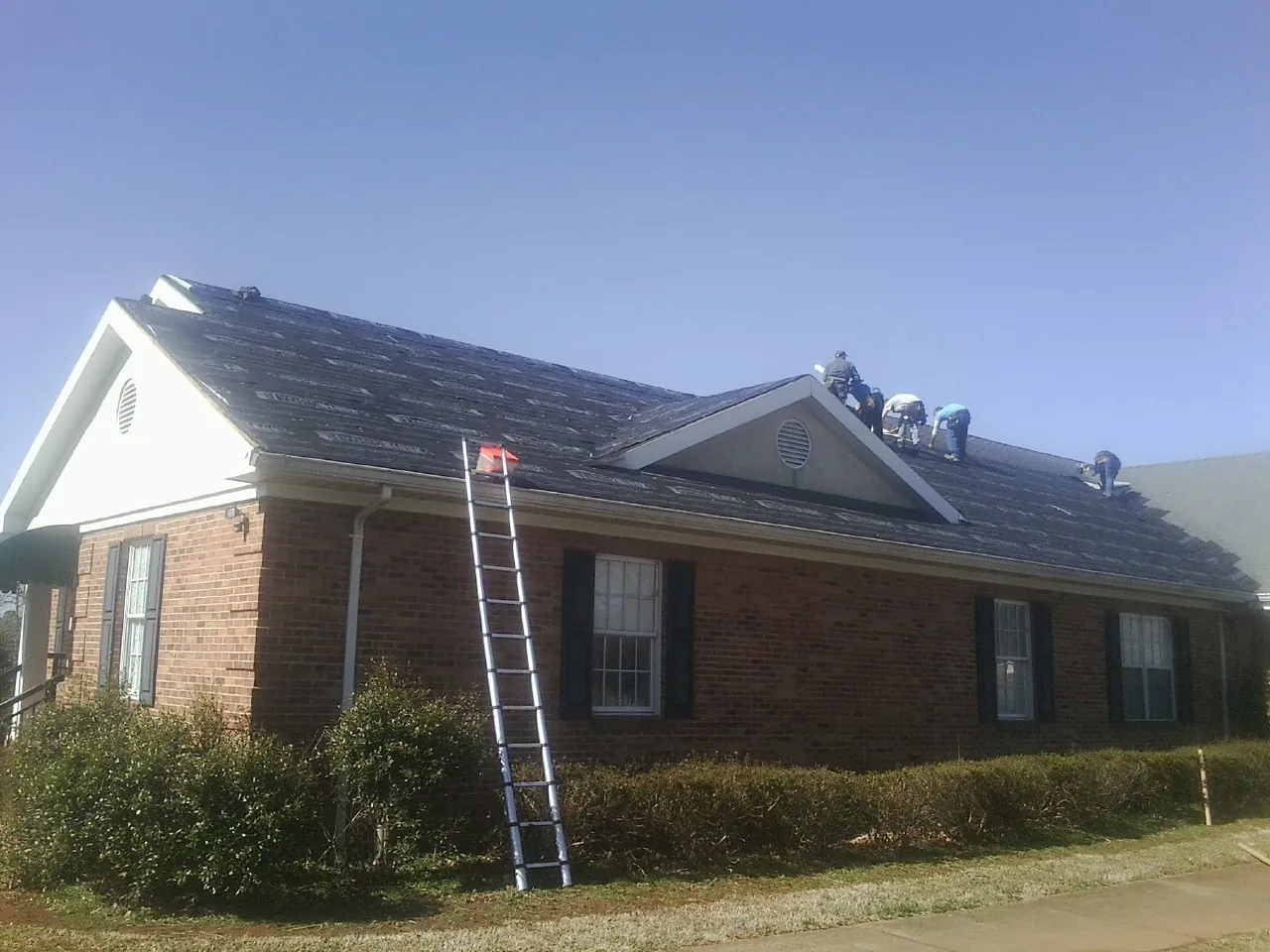 Crew tearing shingles off a brick ranch roof with a ladder set — Metal Roof Repair work by our crew in Norton