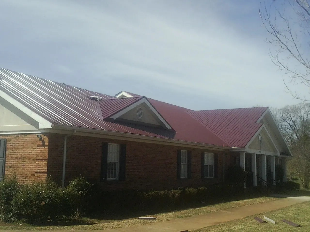 Red metal roof with gabled entries on a long brick building, from a Hail Damage Roof Repair job in Norton